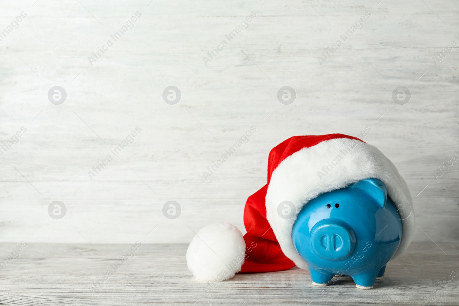 Photo of Piggy bank with Santa hat on table. Space for text