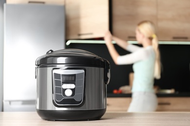 Modern multi cooker and blurred woman on background, space for text