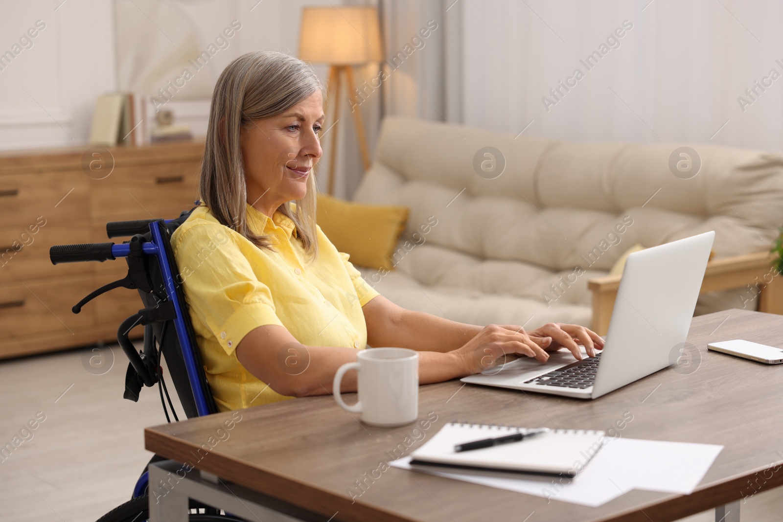 Photo of Woman in wheelchair using laptop at table in home office