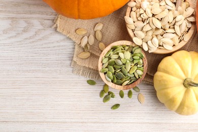 Photo of Bowls with seeds and fresh pumpkins on light wooden table, flat lay. Space for text
