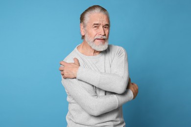 Senior man suffering from pain in arms on light blue background. Arthritis symptoms