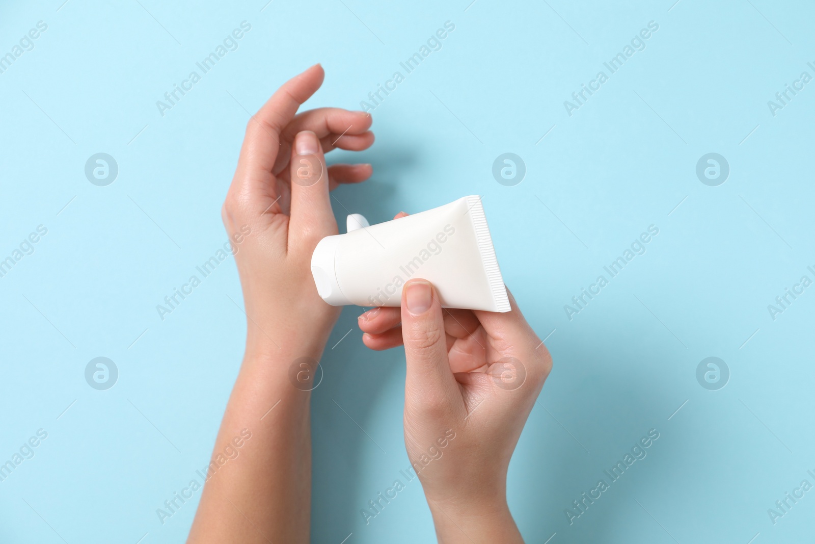 Photo of Woman applying cosmetic cream from tube onto her hand on light blue background, top view