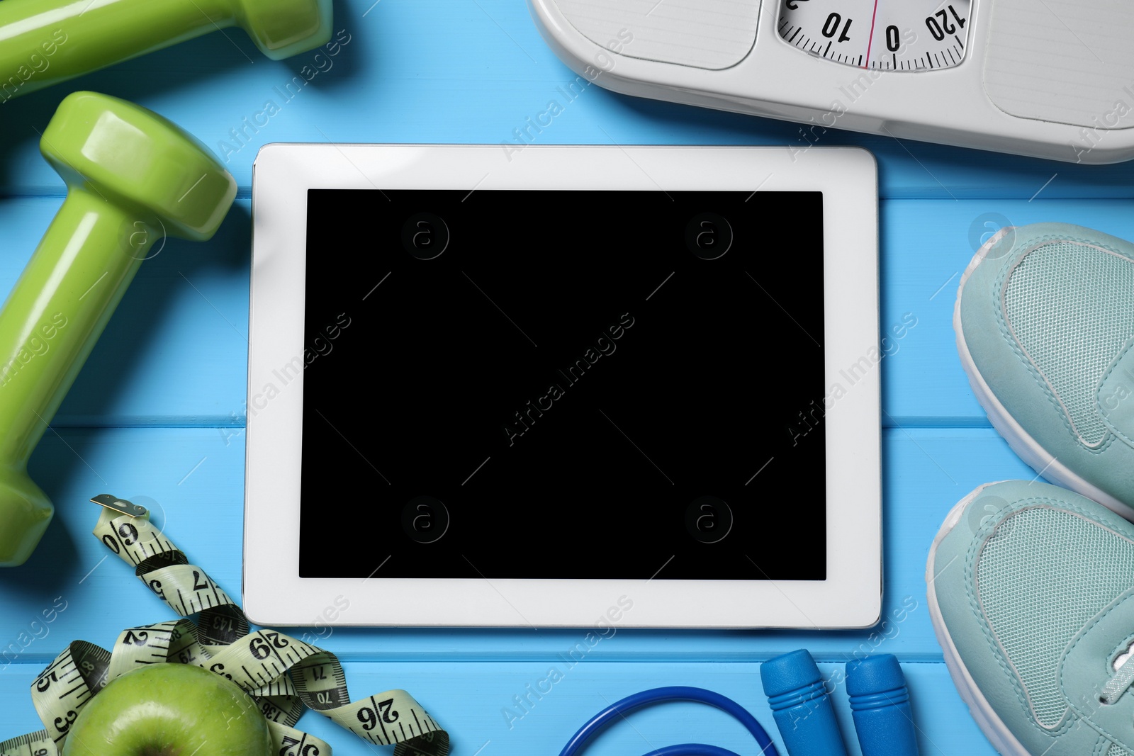 Photo of Tablet, sneakers and sports equipment on light blue wooden table, flat lay. Personal training