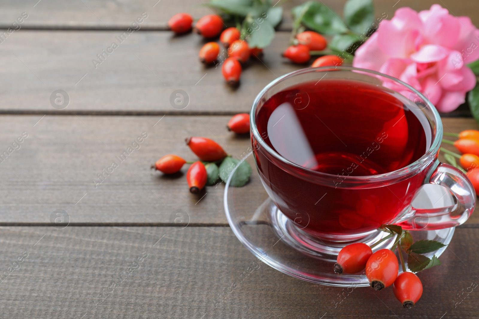 Photo of Aromatic rose hip tea and fresh berries on wooden table, space for text