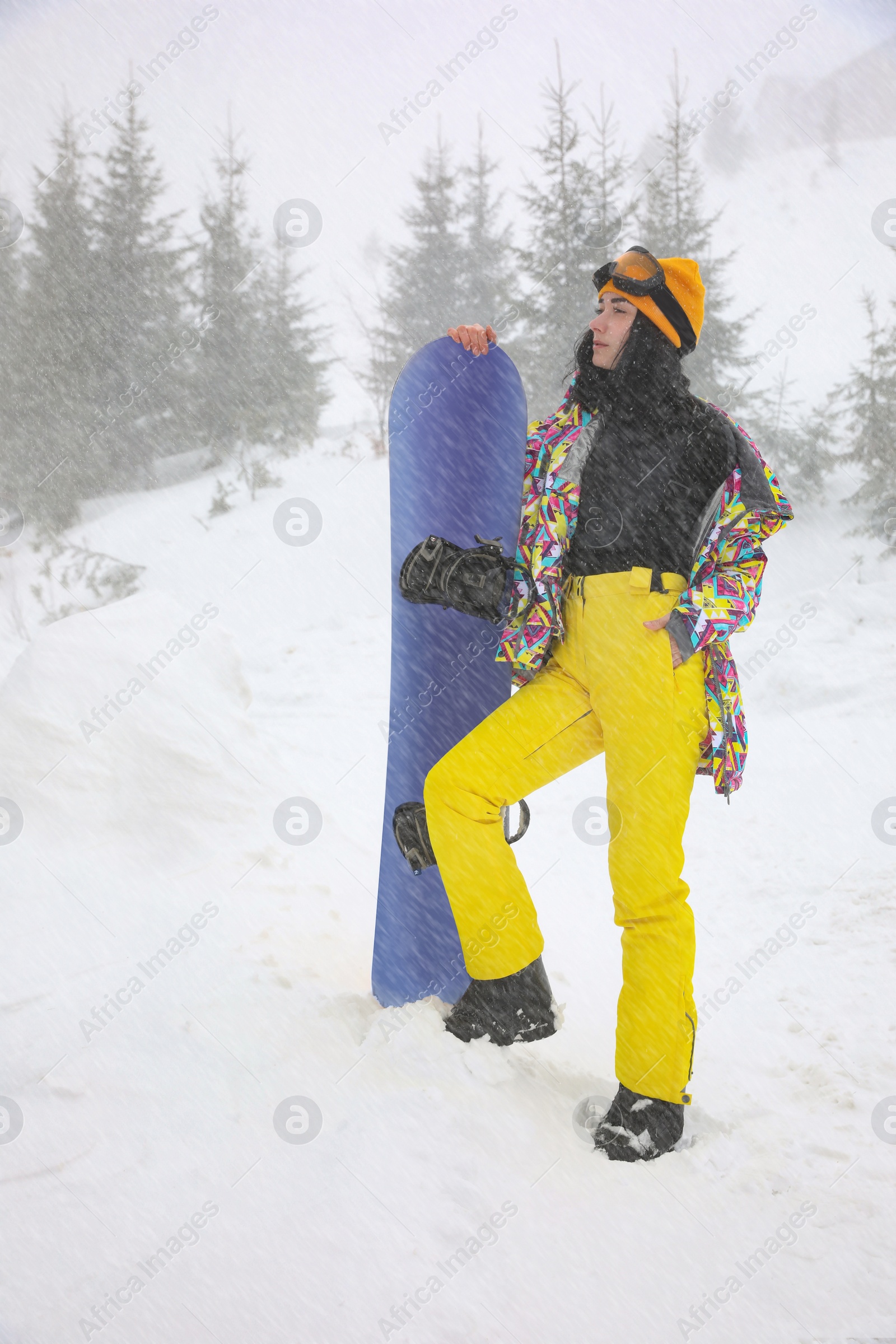 Photo of Young woman with snowboard wearing winter sport clothes outdoors