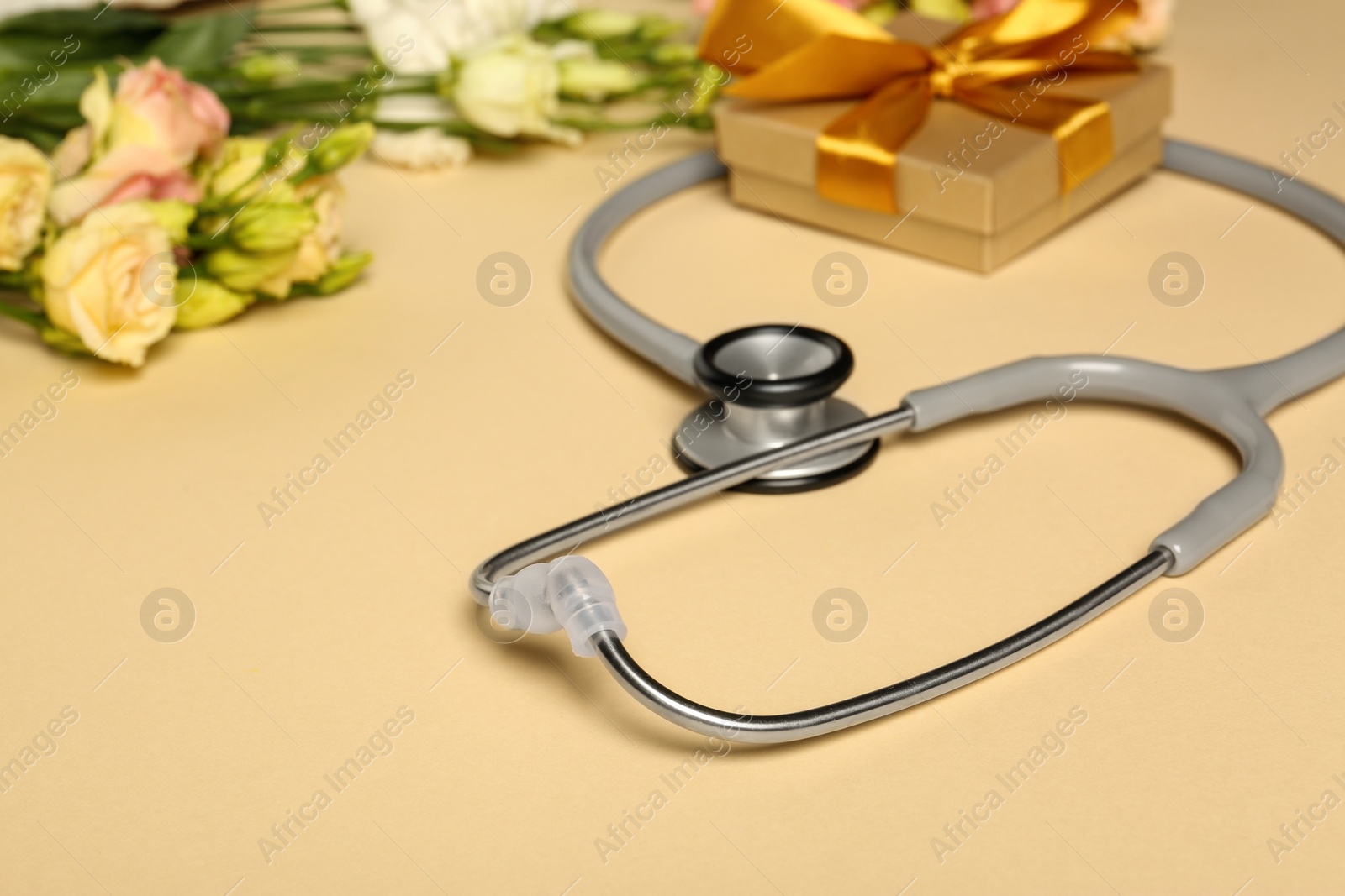 Photo of Stethoscope, gift box and eustoma flowers on beige background. Happy Doctor's Day
