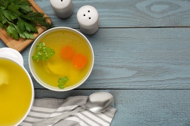Photo of Delicious chicken bouillon with carrot and parsley on grey wooden table, flat lay. Space for text