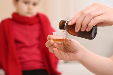Photo of Mother pouring cough syrup into measuring cup for her daughter indoors, focus on hands