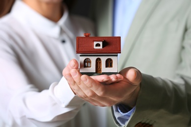 Photo of Young couple holding house model, closeup. Home insurance