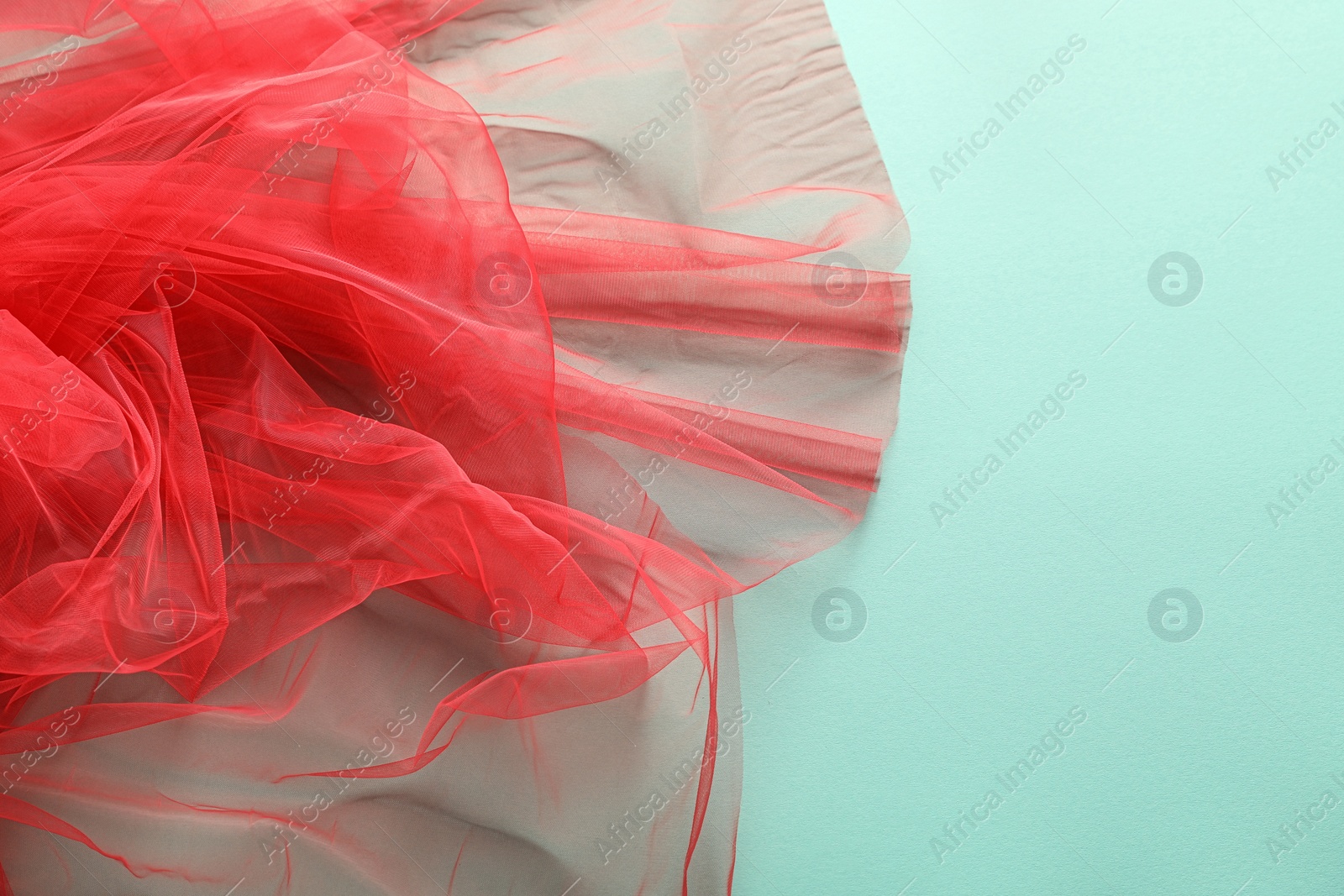 Photo of Beautiful red tulle fabric on turquoise background, closeup