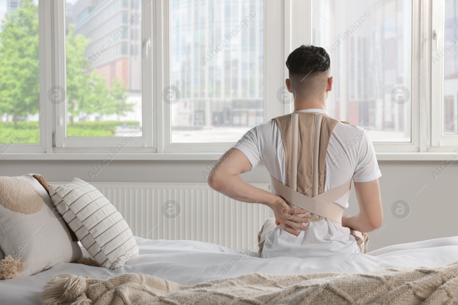 Photo of Man with orthopedic corset sitting in room, back view