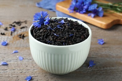 Photo of Bowl with dry tea leaves and cornflower on wooden table, closeup