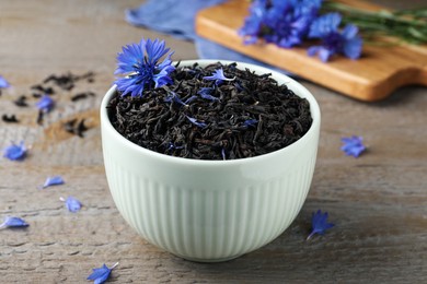 Bowl with dry tea leaves and cornflower on wooden table, closeup