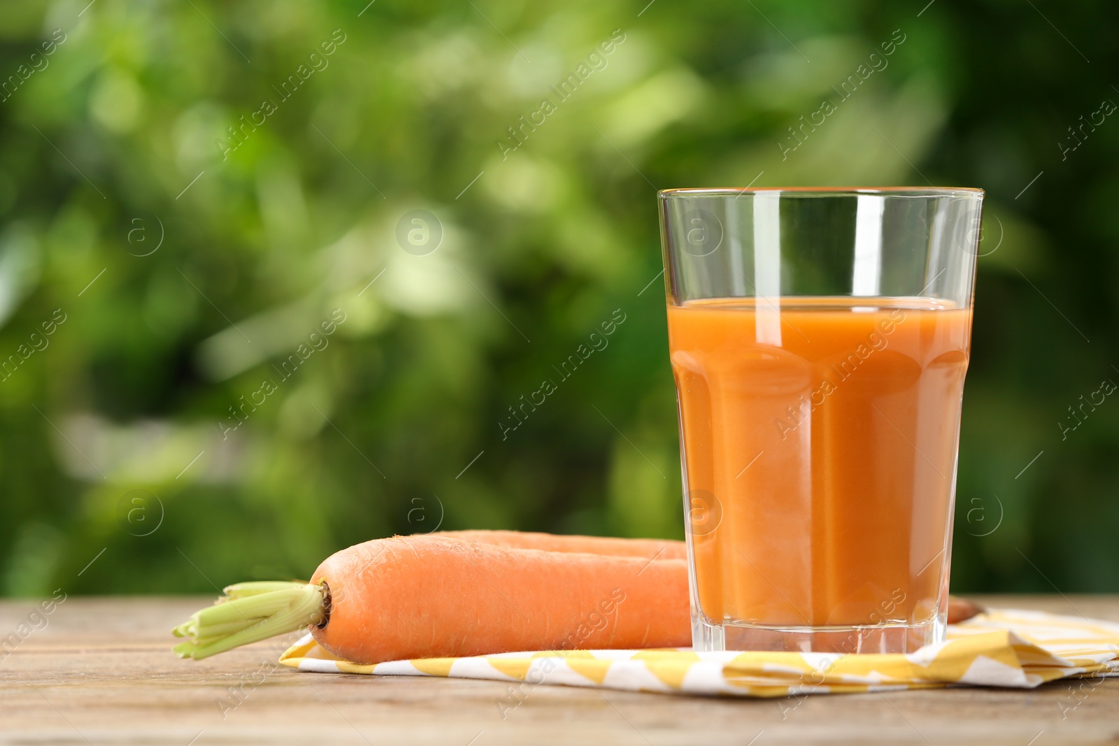 Photo of Glass of carrot drink on wooden table against blurred background, space for text