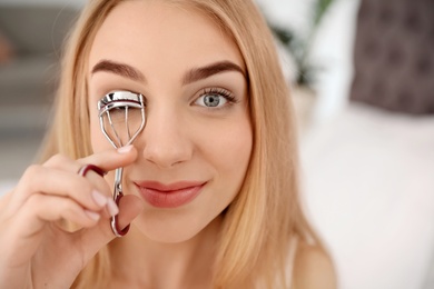 Photo of Young woman curling her eyelashes at home