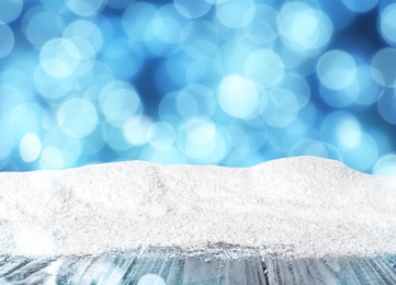 Image of Wooden surface with heap of snow and blurred Christmas lights on background, bokeh effect 