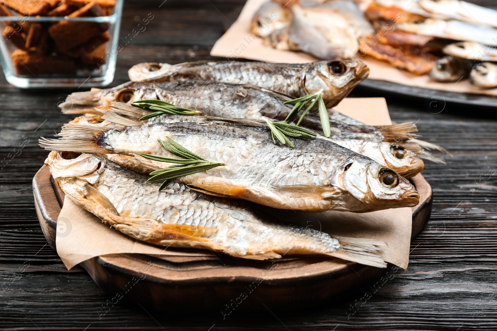 Photo of Tasty dried fish with rosemary on black wooden table