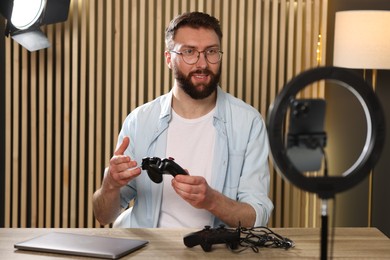 Smiling technology blogger with game controller recording video review at home