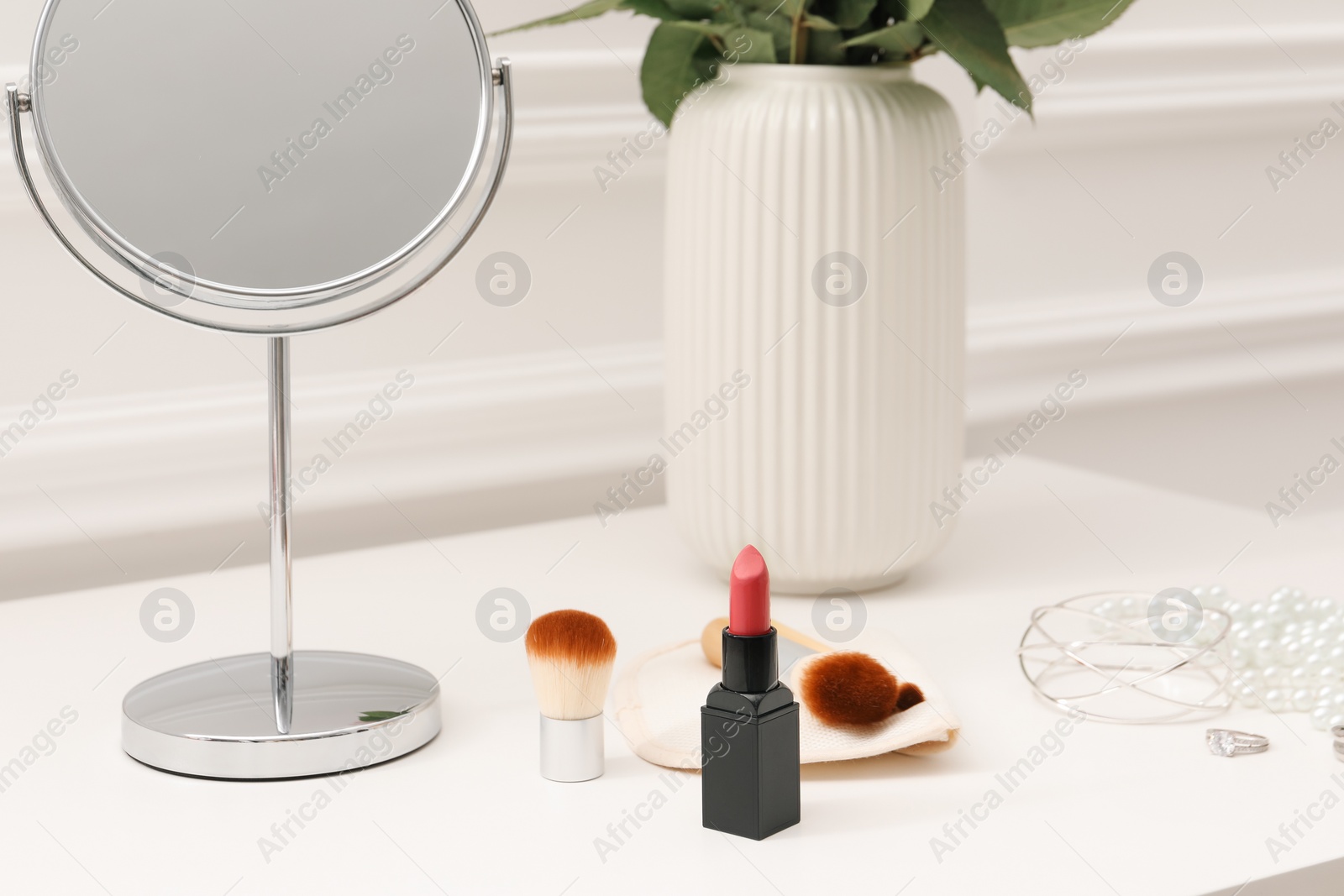 Photo of Mirror, cosmetic products, jewelry and vase with flowers on white dressing table, closeup