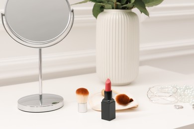 Mirror, cosmetic products, jewelry and vase with flowers on white dressing table, closeup