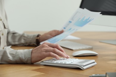 Professional accountant using calculator at wooden desk in office, closeup