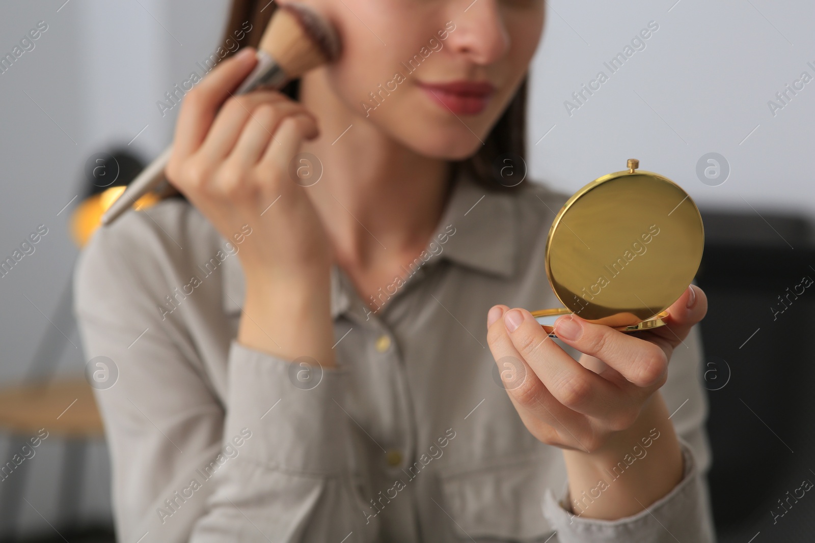 Photo of Young woman with cosmetic pocket mirror doing makeup indoors, closeup