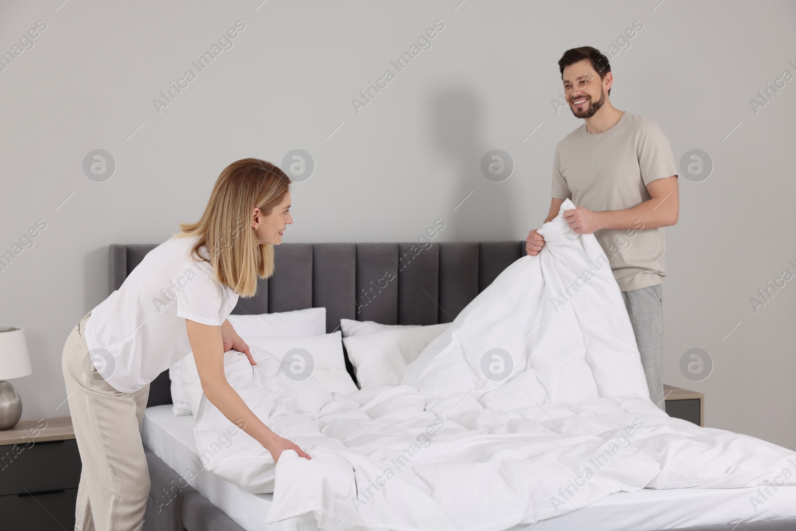 Photo of Couple changing bed linens in room. Domestic chores