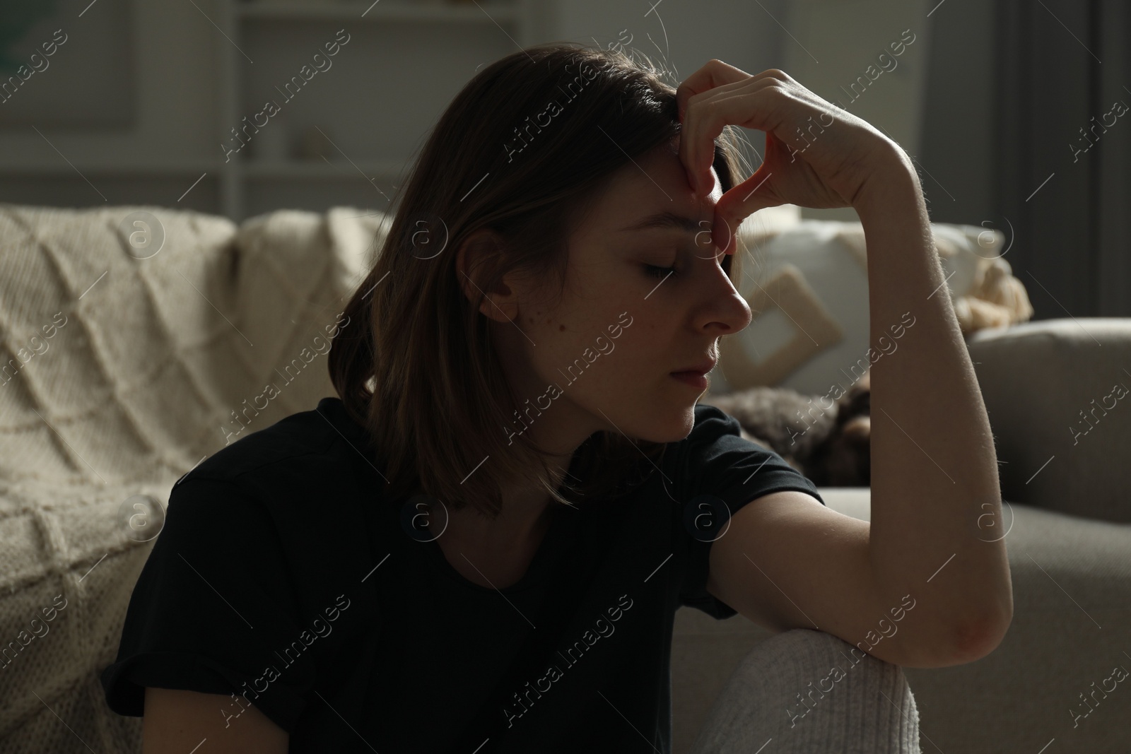 Photo of Sad young woman near sofa at home