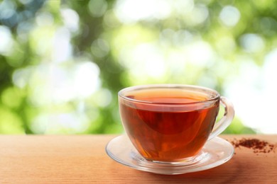 Cup of hot freshly brewed rooibos tea on wooden table outdoors