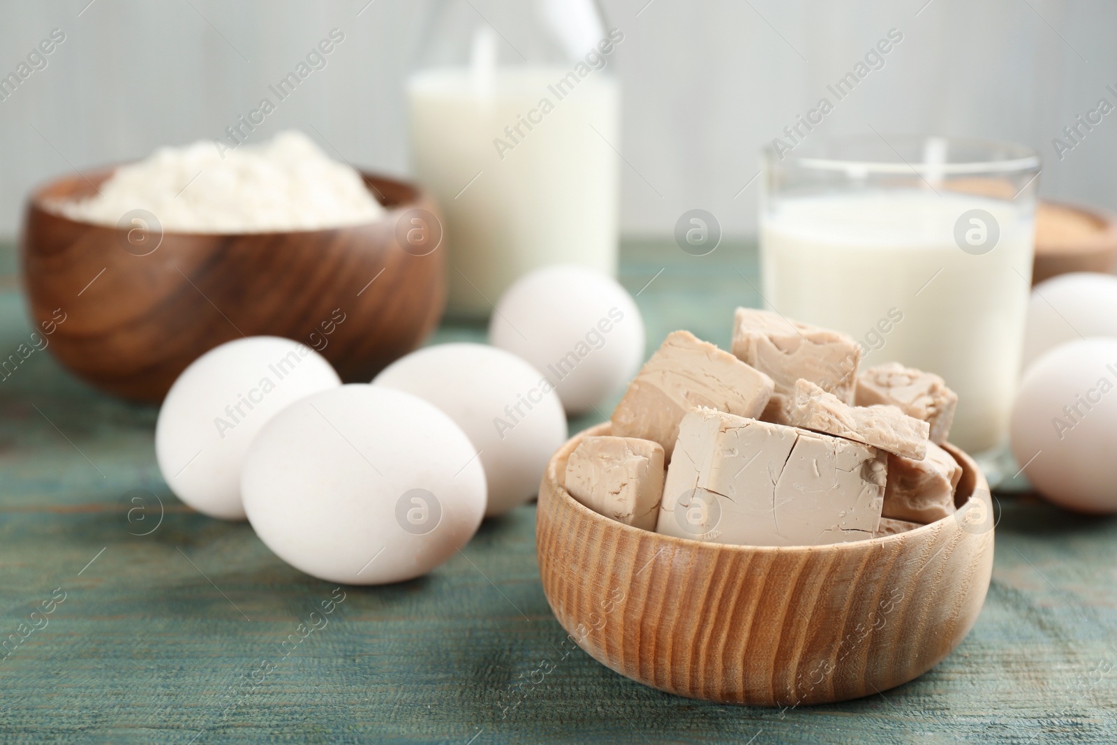 Photo of Pieces of compressed yeast near ingredients for dough on blue wooden table