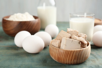 Photo of Pieces of compressed yeast near ingredients for dough on blue wooden table