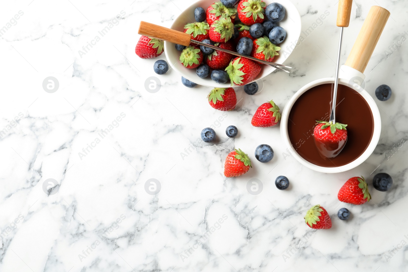 Photo of Dipping strawberry into fondue pot with chocolate on white marble table, flat lay. Space for text