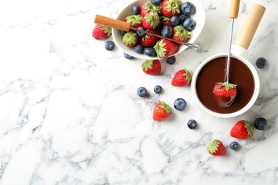 Photo of Dipping strawberry into fondue pot with chocolate on white marble table, flat lay. Space for text