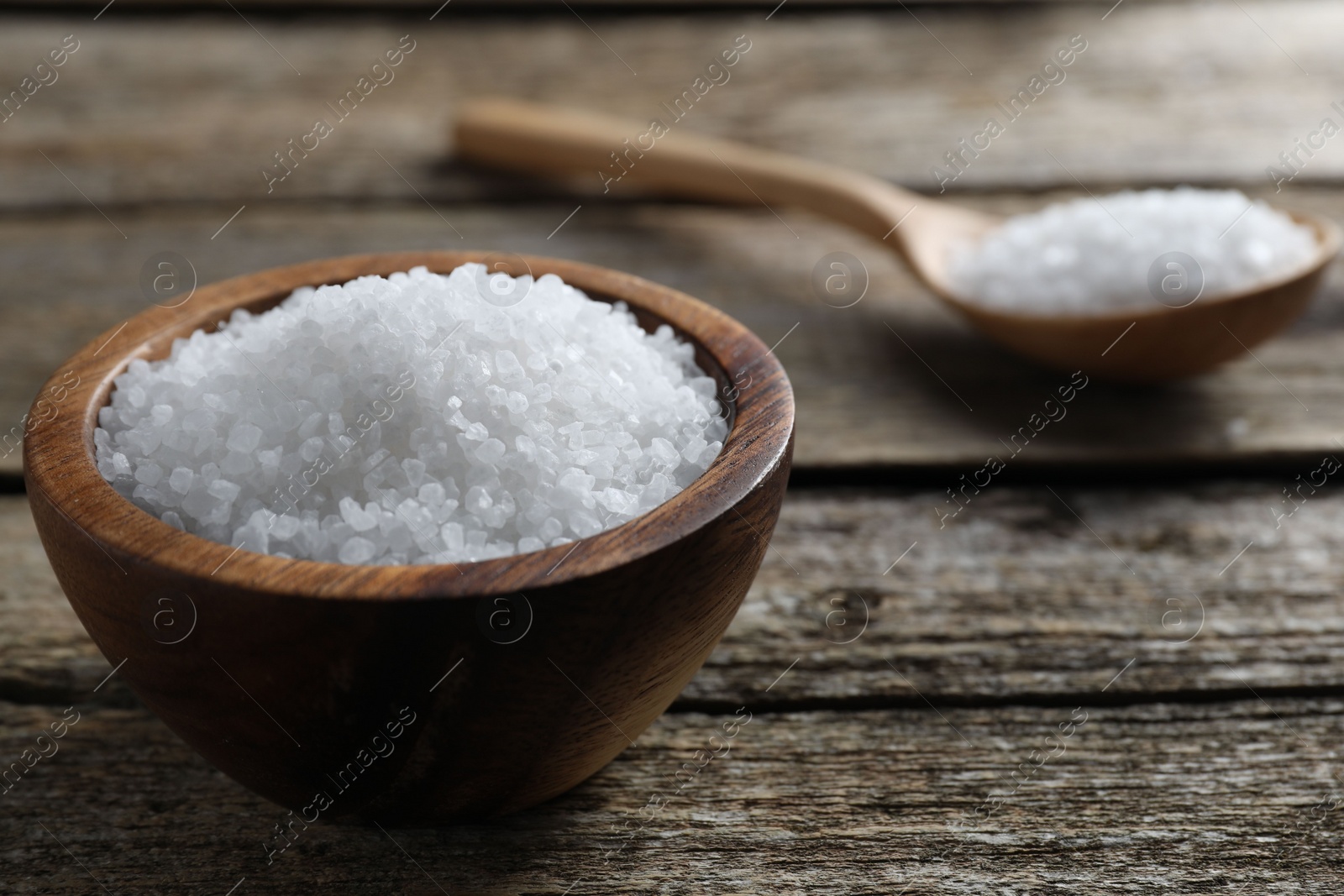 Photo of Organic salt in bowl and spoon on wooden table, closeup. Space for text