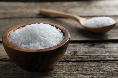 Photo of Organic salt in bowl and spoon on wooden table, closeup. Space for text