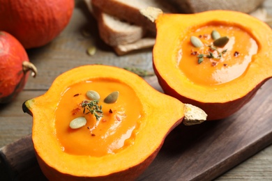 Photo of Tasty cream soup in pumpkin halves on wooden table, closeup