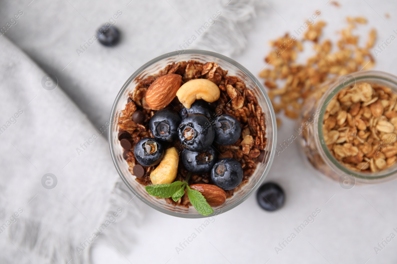 Photo of Tasty granola with berries, nuts and mint in glass on light table, top view