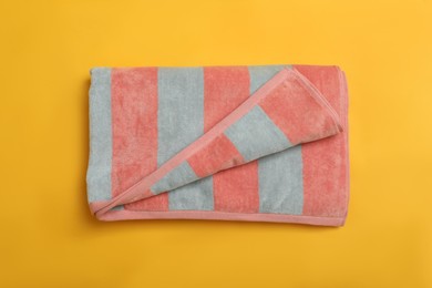 Folded striped beach towel on yellow background, top view