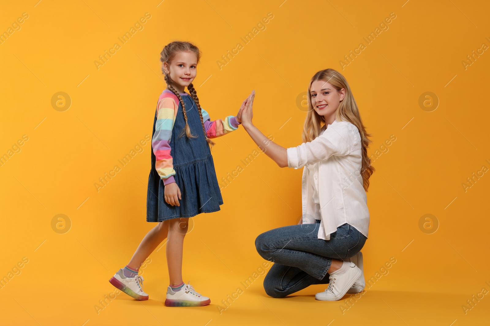 Photo of Mother and daughter giving high five on orange background