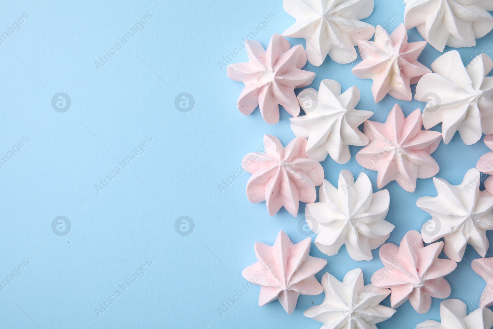 Photo of Tasty meringue cookies on light blue background, flat lay. Space for text