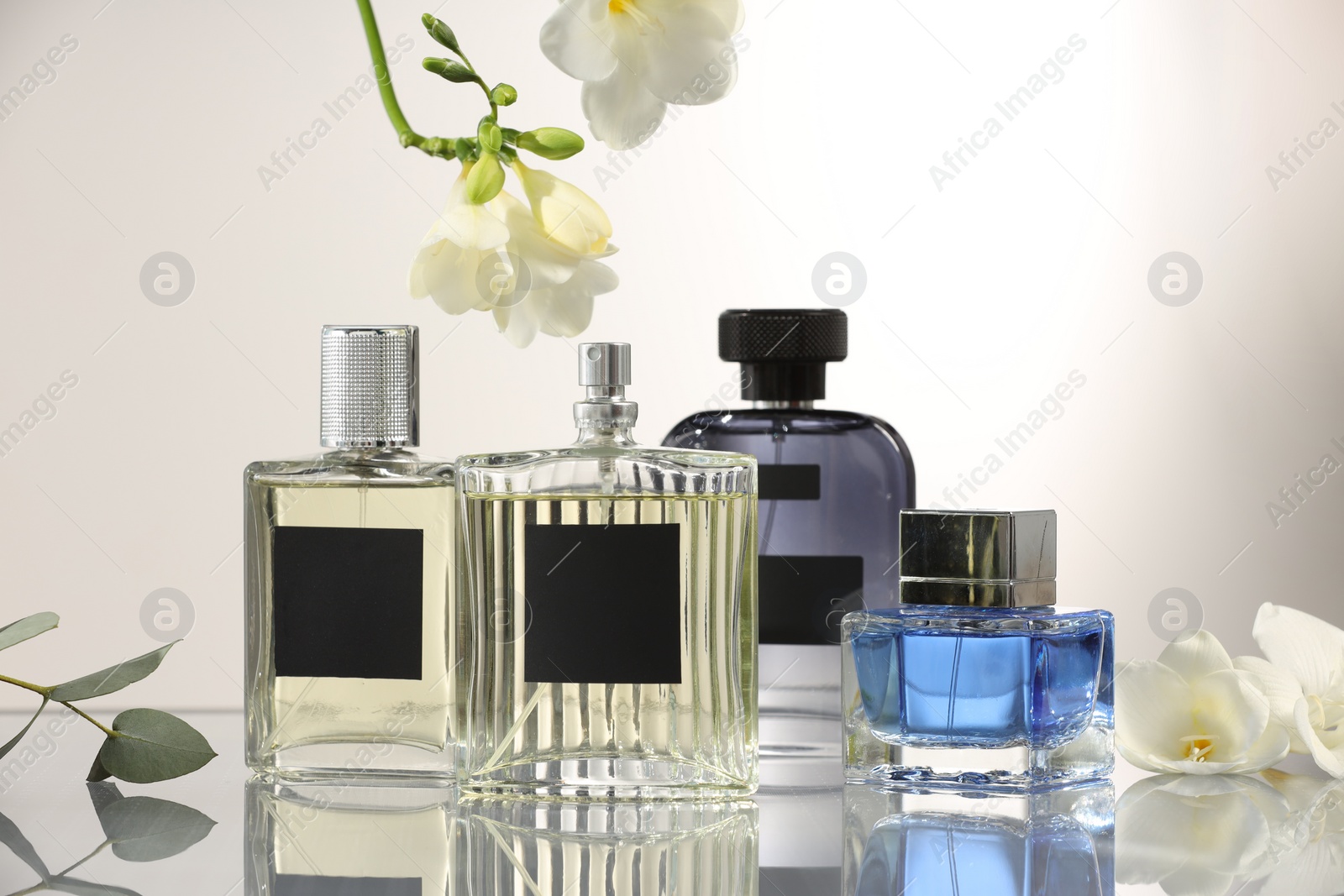 Photo of Luxury perfumes and floral decor on mirror surface against light grey background