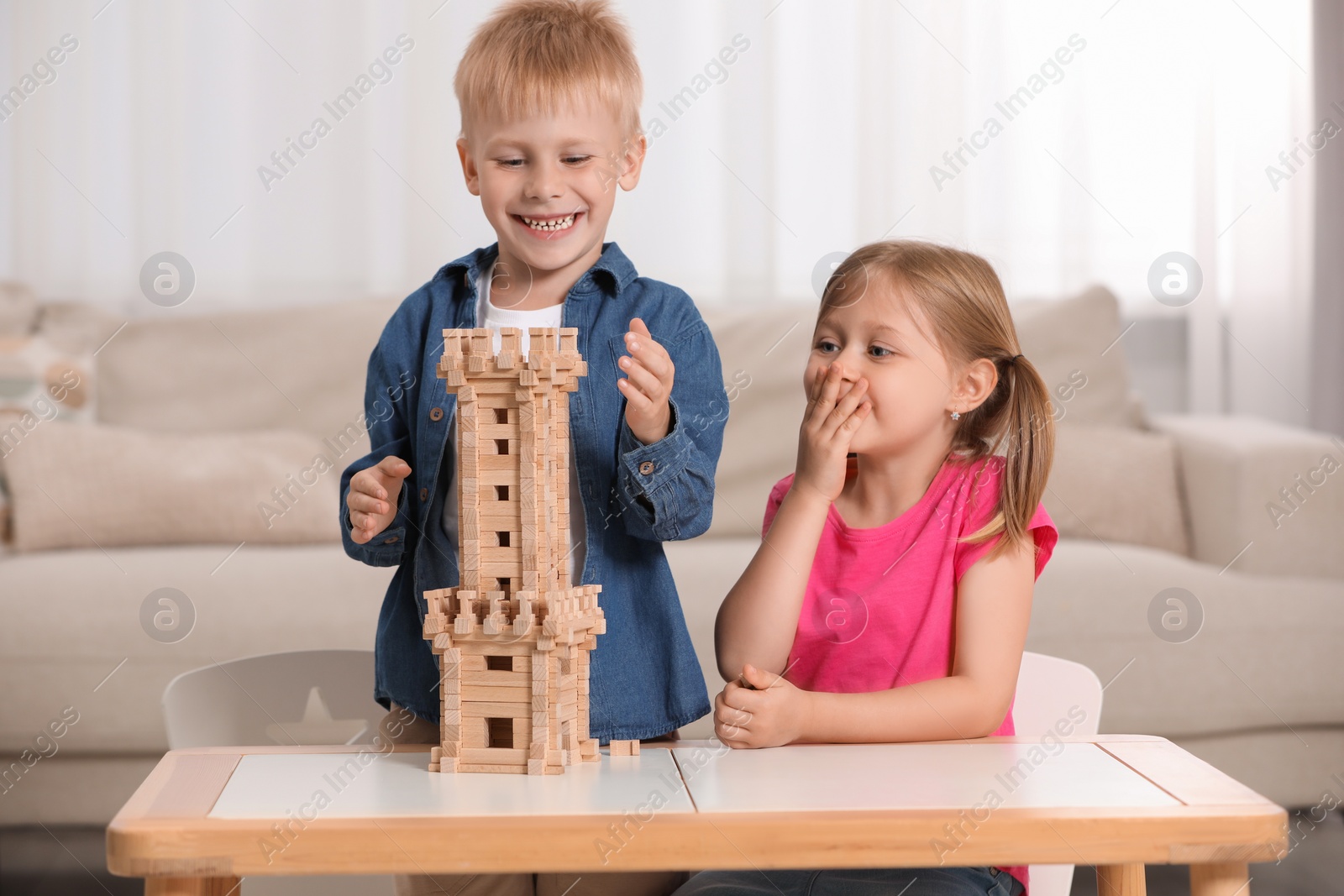 Photo of Little girl and boy playing with wooden tower at table indoors. Children's toy