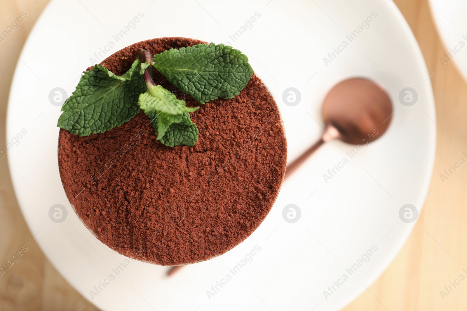 Photo of Tasty tiramisu and mint in glass on light wooden table, top view