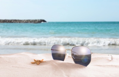 Starfish and stylish sunglasses on sandy beach near sea