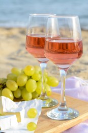Photo of Glasses with rose wine and snacks for beach picnic on sandy seashore, closeup