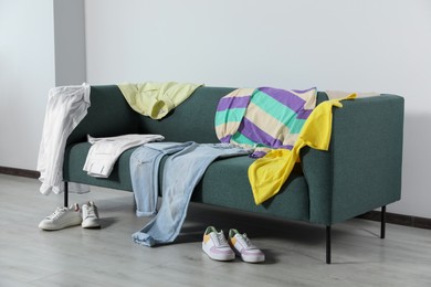 Photo of Messy pile of clothes on sofa and shoes in living room