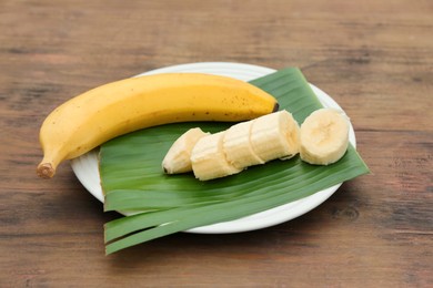 Photo of Plate with delicious bananas and fresh leaf on wooden table
