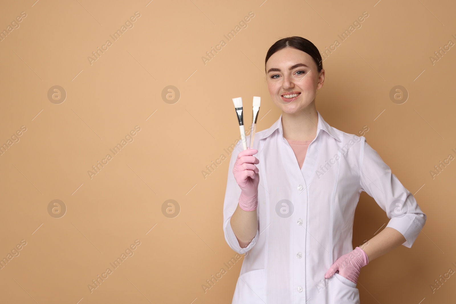 Photo of Cosmetologist with cosmetic brushes on beige background, space for text