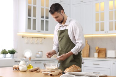 Photo of Making bread. Man putting salt into bowl with flour at wooden table in kitchen