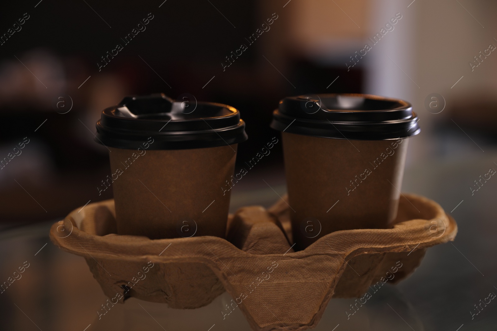 Photo of Takeaway coffee cups with cardboard holder on glass table indoors, closeup